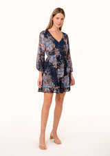 [Color: Navy/Dusty Blue] A full body front facing image of a blonde model wearing a bohemian fall chiffon mini dress in a blue floral print. Designed with metallic clip dot details throughout, sheer long sleeves, a v neckline, an elastic waist, a decorative button front, and a double layered tiered skirt. 