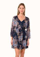 [Color: Navy/Dusty Blue] A front facing image of a blonde model wearing a bohemian fall chiffon mini dress in a blue floral print. Designed with metallic clip dot details throughout, sheer long sleeves, a v neckline, an elastic waist, a decorative button front, and a double layered tiered skirt. 