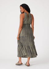 [Color: Olive] A back facing image of a brunette model wearing an olive green bohemian maxi dress in a soft pink vintage wash. With a ruffle trimmed halter neckline, a smocked elastic waist, a tiered long skirt, and a back keyhole detail with an adjustable tie.
