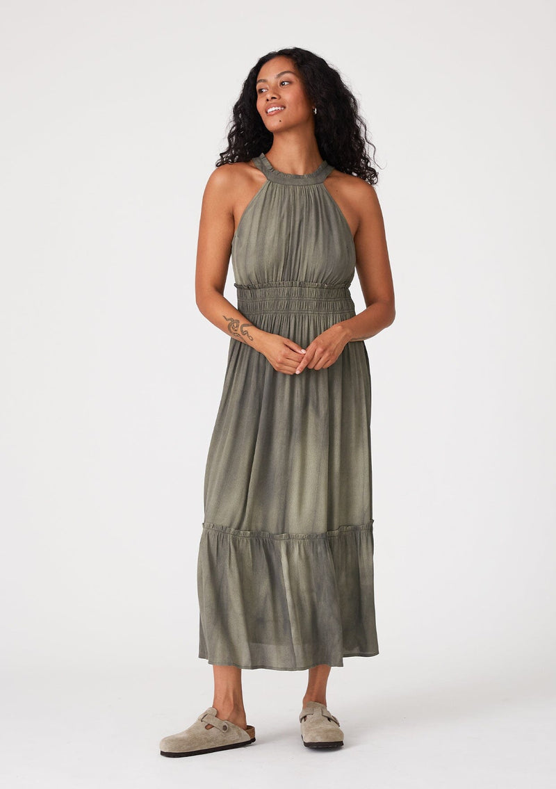 [Color: Olive] A front facing image of a brunette model wearing an olive green bohemian maxi dress in a soft pink vintage wash. With a ruffle trimmed halter neckline, a smocked elastic waist, a tiered long skirt, and a back keyhole detail with an adjustable tie.