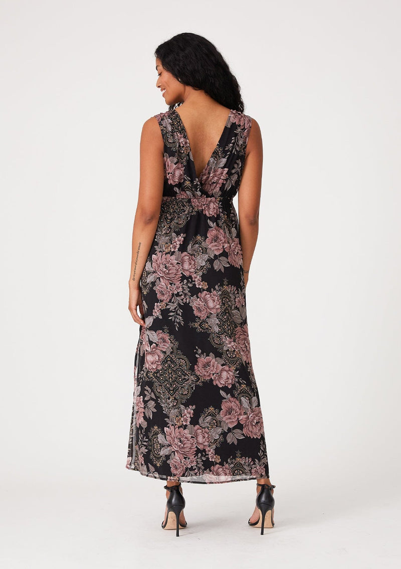 [Color: Black/Dusty Rose] A back facing image of a brunette model wearing a bohemian fall mid length dress designed in a black and pink floral print, with metallic details throughout. With a surplice v neckline, an elastic empire waist, a side slit, and thick tank top straps with tie shoulder details. 