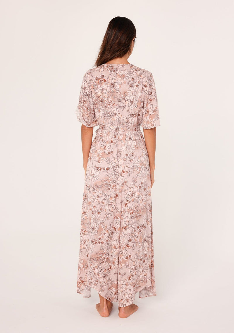 [Color: Dusty Rose/Light Brown] A back facing image of a brunette model wearing a bohemian pink floral maxi dress with short flutter sleeves, a v neckline, a long flowy skirt, and a self tie waist belt. 