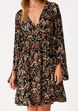 [Color: Black/Taupe] A close up front facing image of a blonde model wearing a bohemian fall mini dress in a bohemian brown print. With an empire waist, a deep v neckline, a relaxed flowy fit, and long bell sleeves with a split wrist detail. 