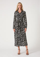 [Color: Black/Natural] A front facing image of a blonde model wearing a bohemian resort maxi shirt dress in a black and off white abstract print. With a self covered button front, long sleeves, a collared neckline, side slits, and an attached waist tie. 