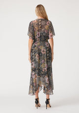 [Color: Black/Dusty Peach] A back facing image of a blonde model wearing a bohemian chiffon maxi dress designed in a black and pink mixed floral print. With short flutter sleeves, a v neckline, a smocked elastic waist, and a long flowy skirt with a tiered asymmetric hemline. 