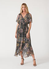 [Color: Black/Dusty Peach] A front facing image of a blonde model wearing a bohemian chiffon maxi dress designed in a black and pink mixed floral print. With short flutter sleeves, a v neckline, a smocked elastic waist, and a long flowy skirt with a tiered asymmetric hemline. 