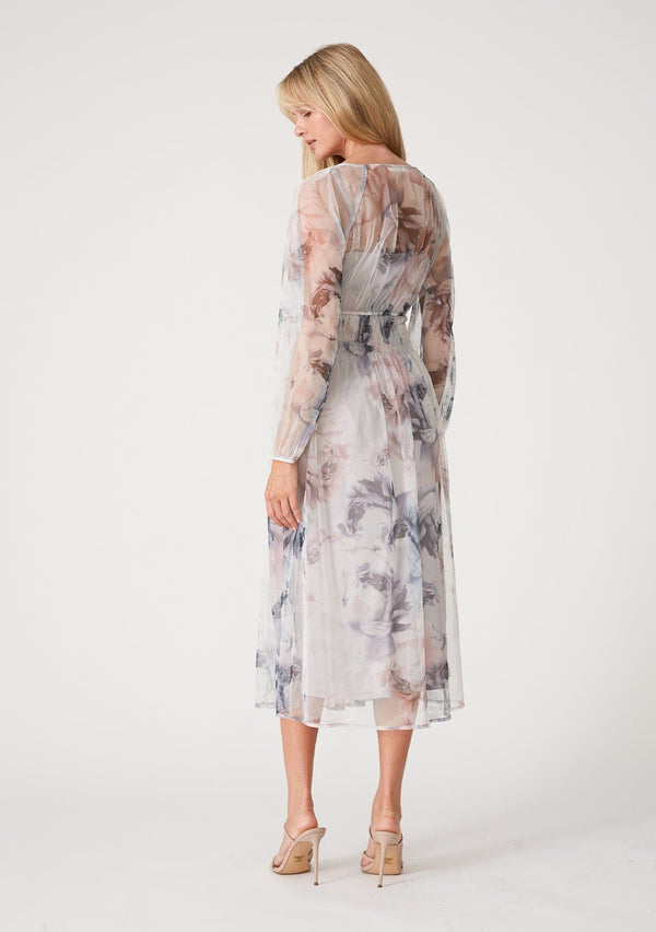 [Color: Grey/Dusty Rust] A back facing image of a blonde model wearing a bohemian resort maxi dress crafted from sheer mesh tulle, designed in a grey and dusty rust floral print. With long raglan sleeves, a v neckline, and a smocked elastic waist. 