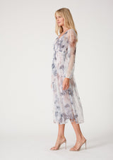 [Color: Grey/Dusty Rust] A side facing image of a blonde model wearing a bohemian resort maxi dress crafted from sheer mesh tulle, designed in a grey and dusty rust floral print. With long raglan sleeves, a v neckline, and a smocked elastic waist. 