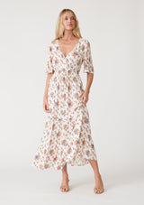 [Color: Natural/Rust] A front facing image of a blonde model wearing a classic bohemian maxi dress in an off white and pink floral print. With short flutter sleeves, a surplice v neckline, a smocked elastic waist, a drawstring tie waist, and a long flowy tiered skirt. 