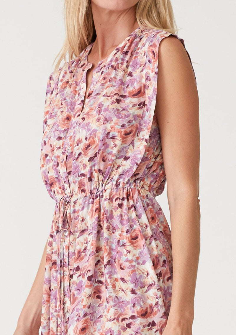 [Color: Dusty Purple/Taupe] A close up side facing image of a blonde model wearing a pink and purple floral print sleeveless mini dress. With a round neckline, a self covered button front, a tiered mini skirt, and a drawstring waist with ties. 