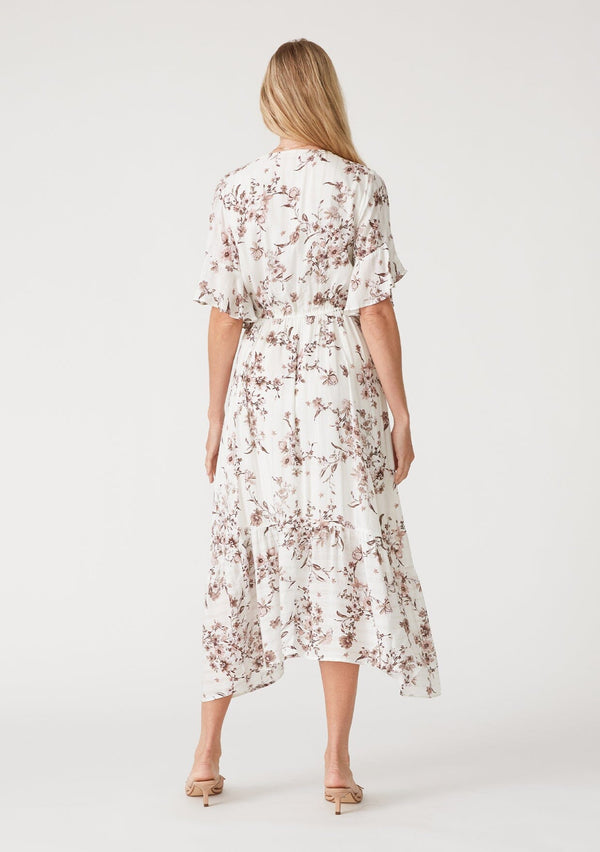 [Color: Ivory/Taupe] A back facing image of a blonde model wearing an ivory and taupe floral print bohemian maxi dress with sparkly metallic thread detail. With short flutter sleeves, a long tiered skirt, a surplice v neckline, and an adjustable drawstring waist. 