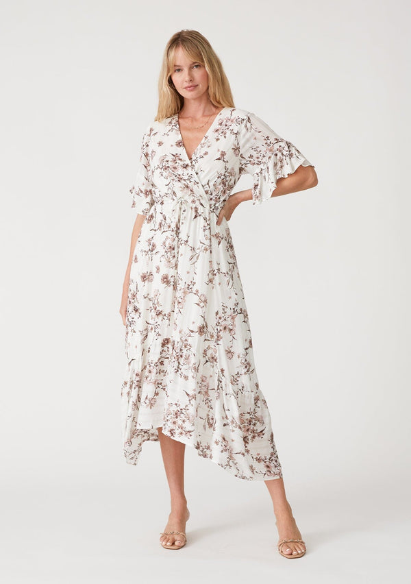 [Color: Ivory/Taupe] A front facing image of a blonde model wearing an ivory and taupe floral print bohemian maxi dress with sparkly metallic thread detail. With short flutter sleeves, a long tiered skirt, a surplice v neckline, and an adjustable drawstring waist. 