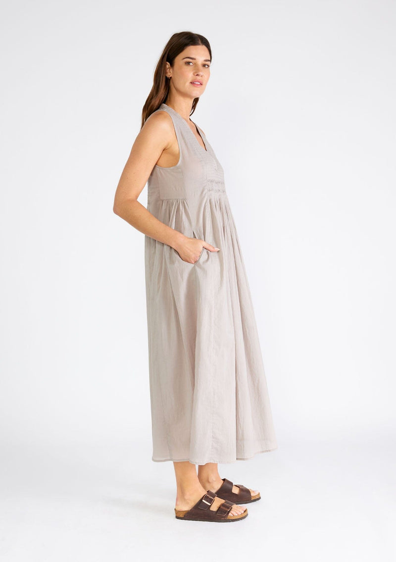 [Color: Grey] A side facing image of a brunette model wearing a lightweight bohemian sleeveless maxi tent dress in grey. With a v neckline, pleated details, and side pockets.