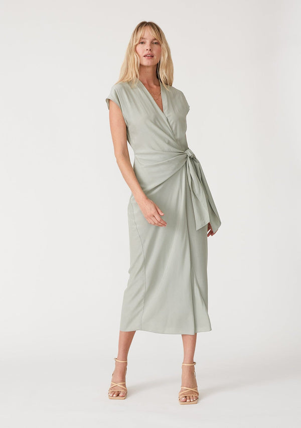 [Color: Pistachio] A front facing image of a blonde model wearing a light green maxi length wrap dress. With short cap sleeves, a deep v neckline, and a side tie waist closure. 