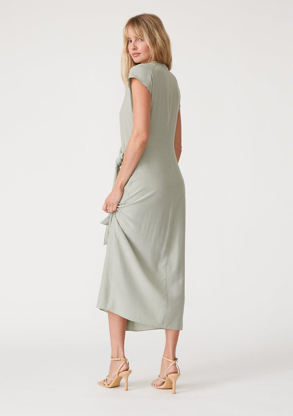 [Color: Pistachio] A back facing image of a blonde model wearing a light green maxi length wrap dress. With short cap sleeves, a deep v neckline, and a side tie waist closure. 