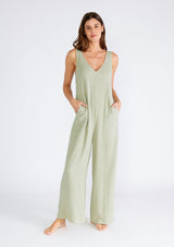 [Color: Dusty Sage] A full body front facing image of a brunette model wearing a bohemian sleeveless jumpsuit in a dusty sage green. With adjustable tank top straps, a v neckline, a long wide leg, side pockets, and back patch pockets. 