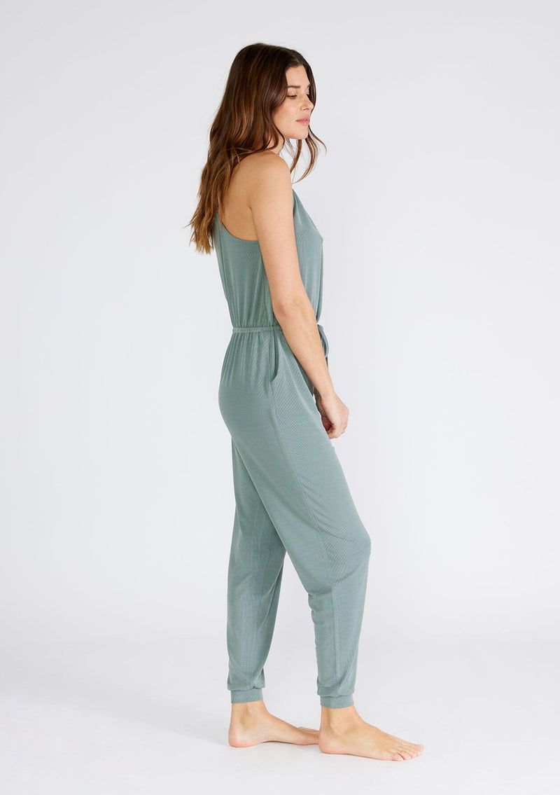 [Color: Slate Green] A side facing image of a brunette model wearing a seafoam green ribbed knit sleeveless jumpsuit. With spaghetti straps, a surplice v neckline, side pockets, and a drawstring tie waist. 