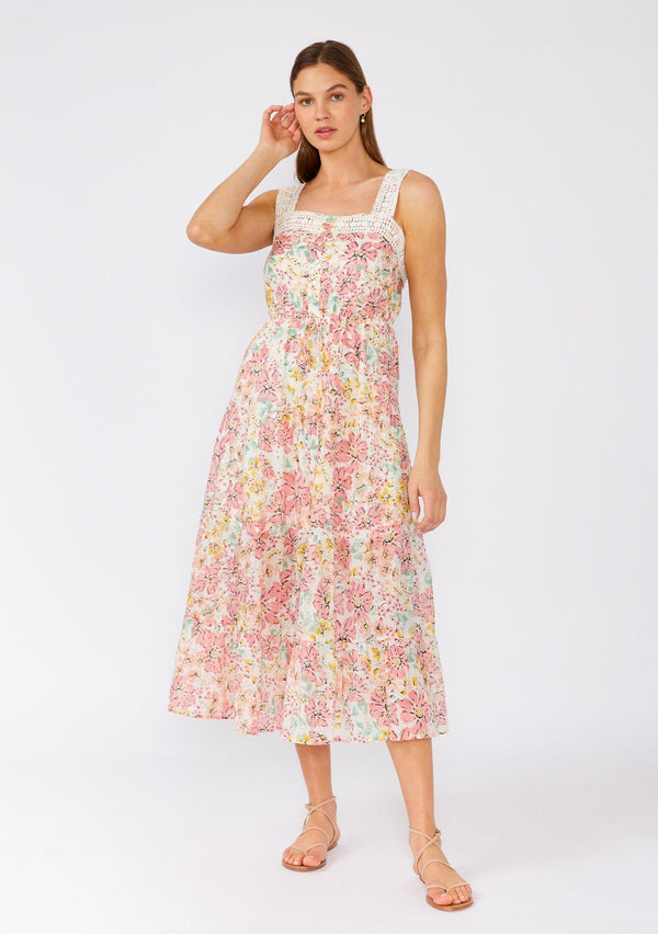 [Color: Natural/Peach Blossom] A front facing image of a brunette model wearing a bohemian pink floral mid length dress. A sleeveless summer dress with adjustable tank top straps, a square neckline, a flowy tiered skirt, an adjustable drawstring tie waist, and lace trim. 