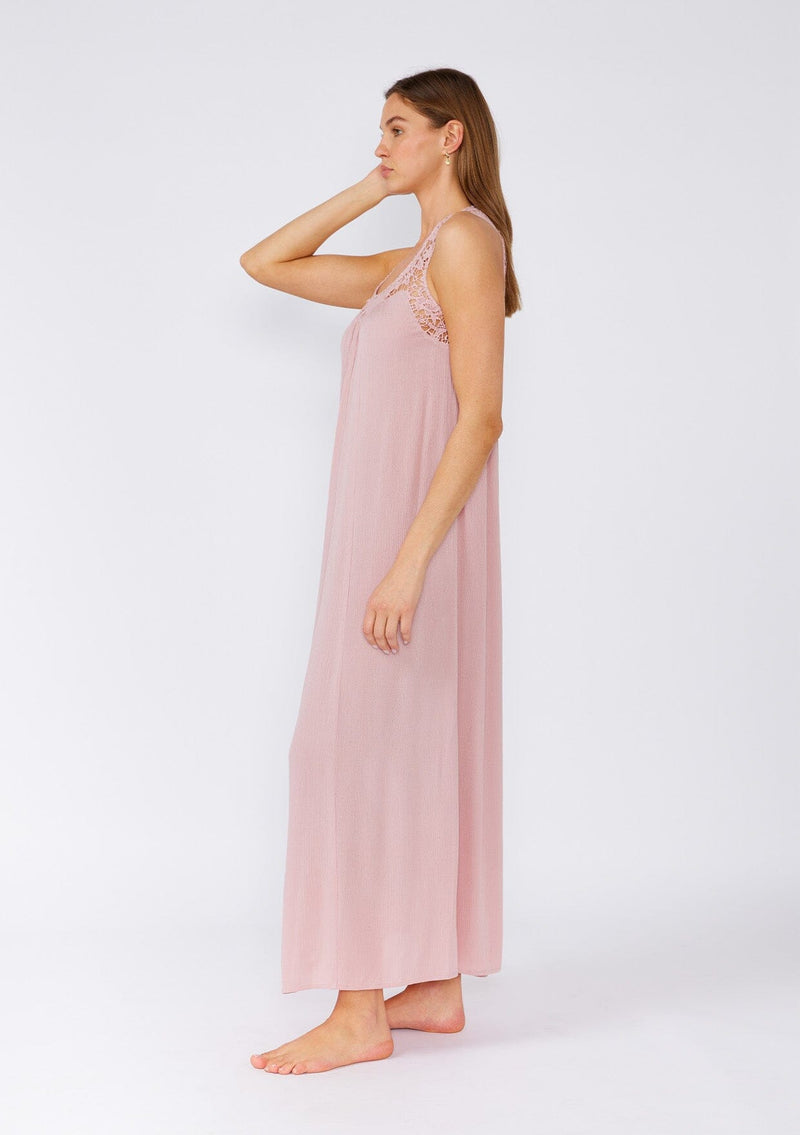 [Color: Dusty Rose] A side facing image of a brunette model wearing a flowy sleeveless bohemian maxi dress in dusty pink. With a crochet top, a scooped neckline, and an open back detail. 