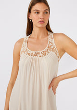 [Color: Natural] A close up front facing image of a brunette model wearing a flowy sleeveless bohemian maxi dress in ivory. With a crochet top, a scooped neckline, and an open back detail. 