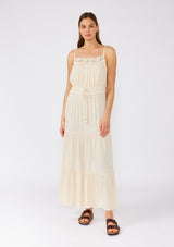 [Color: Natural] A full body front facing image of a brunette model wearing an off white sleeveless maxi dress. With adjustable spaghetti straps, a straight neckline, crochet trim, a tassel tie drawstring waist, and a ruffle trimmed tiered skirt. 