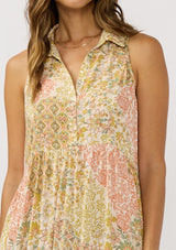 [Color: Dusty Peach/Rust] A detail image of a brunette model wearing a bohemian sleeveless maxi dress designed in a peach and rust floral print. With a collared neckline, a self covered button front top, a long tiered skirt, and side pockets. 