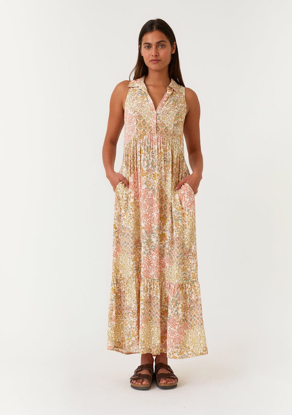 [Color: Dusty Peach/Rust] A front facing image of a brunette model wearing a bohemian sleeveless maxi dress designed in a peach and rust floral print. With a collared neckline, a self covered button front top, a long tiered skirt, and side pockets. 