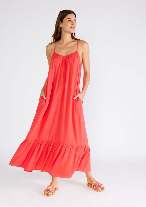 [Color: Hibiscus] A front facing image of a brunette model wearing a red bohemian sleeveless maxi dress. With spaghetti straps, a scoop neckline, side pockets, a long flowy tiered skirt, and a sheer lace racerback detail. 