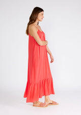[Color: Hibiscus] A side facing image of a brunette model wearing a red bohemian sleeveless maxi dress. With spaghetti straps, a scoop neckline, side pockets, a long flowy tiered skirt, and a sheer lace racerback detail. 