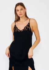 [Color: Black] A close up front facing image of a brunette model wearing a classic black maxi slip dress with lace detail along the neckline. With adjustable spaghetti straps, a scooped neckline, and a long flowy skirt with side slits. 