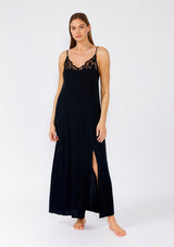 [Color: Black] A front facing image of a brunette model wearing a classic black maxi slip dress with lace detail along the neckline. With adjustable spaghetti straps, a scooped neckline, and a long flowy skirt with side slits. 