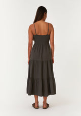 [Color: Lagoon] A back facing image of a brunette model wearing a sleeveless army green mid length spring dress. With adjustable spaghetti straps, a scoop neckline, a tiered skirt, and a half smocked elastic bodice at the back. 