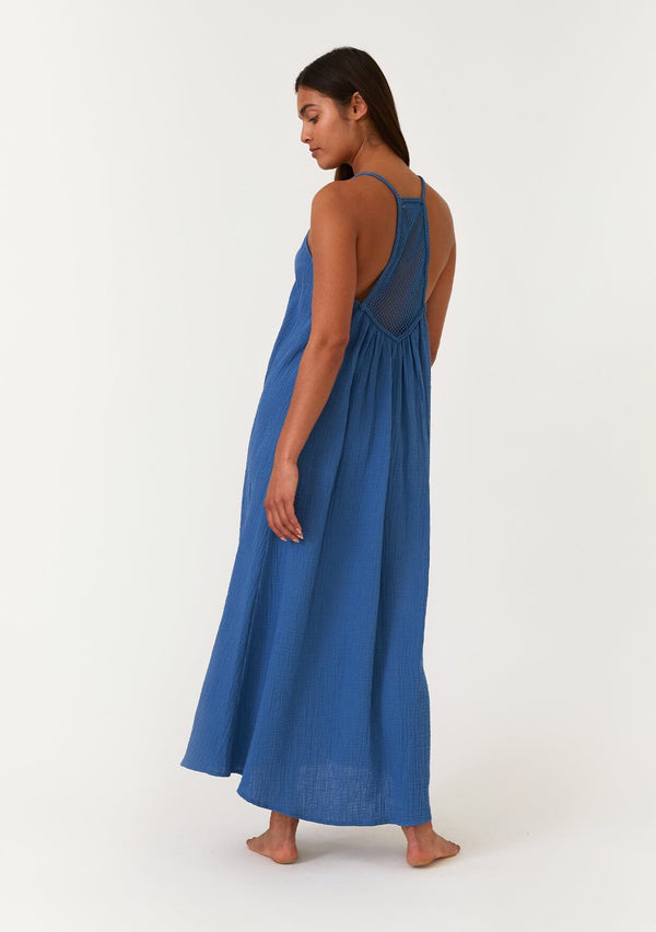 [Color: Ocean] A back facing image of a brunette model wearing a blue bohemian sleeveless maxi dress crafted from cotton gauze. With braided straps, a v neckline, a relaxed, flowy body, and a sheer crochet mesh racerback detail. 