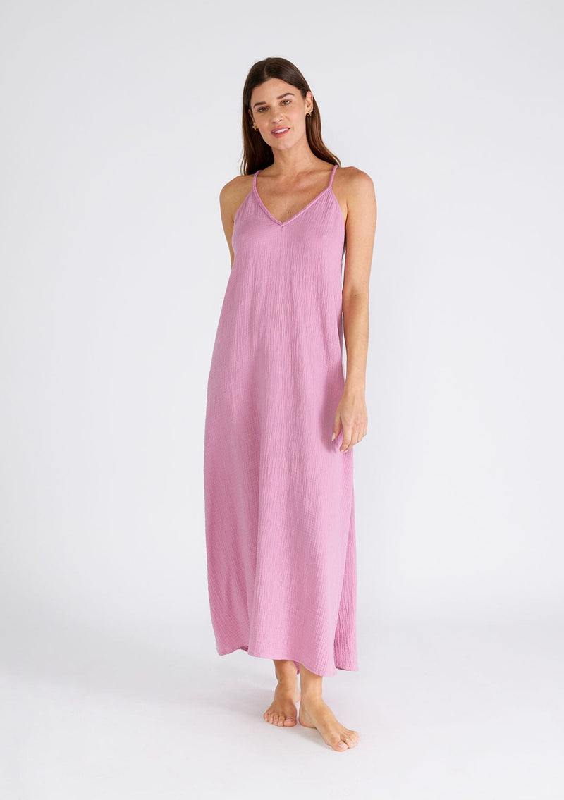 [Color: Orchid] A full body front facing image of a brunette model wearing a light purple bohemian sleeveless maxi dress crafted from cotton gauze. With braided straps, a v neckline, a relaxed, flowy body, and a sheer crochet mesh racerback detail.