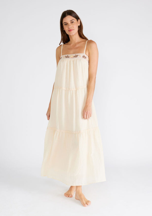 [Color: Light Peach] A front facing image of a brunette model wearing a light peach pink sleeveless maxi dress. A lightweight bohemian style with embroidered detail at the neckline, adjustable spaghetti straps, a lace trimmed tiered skirt, a straight neckline, and a long flowy fit. 