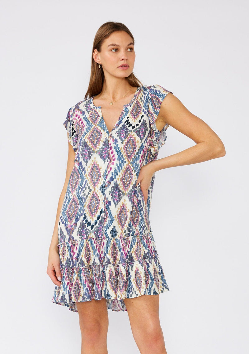 [Color: Natural/Dusty Blue] A front facing image of a brunette model wearing a relaxed and flowy casual mini dress designed in a blue bohemian print. With short flutter sleeves, a v neckline, a button front, a ruffle trimmed tiered skirt, and an ultra relaxed silhouette. 