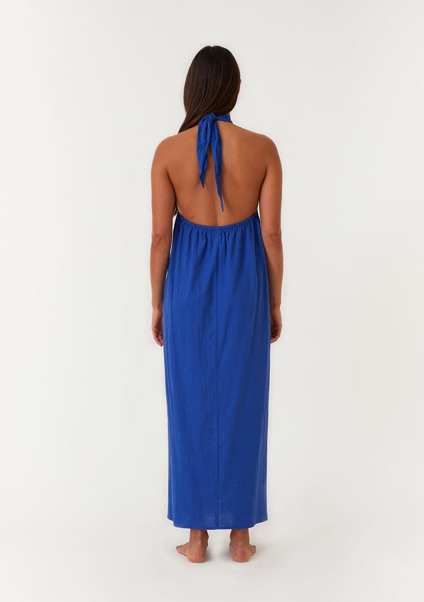 [Color: Cobalt] A back facing image of a brunette model wearing a bright cobalt blue halter maxi dress. With a twist front halter neckline, adjustable tie, front slit, and sexy open back. Perfect for the beach or the pool. 