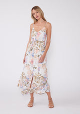 [Color: Off White/Periwinkle] A front facing image of a blonde model wearing a dreamy bohemian mid length sleeveless dress in an off white and periwinkle blue floral print. With adjustable spaghetti straps, a v neckline, a tiered flowy skirt, a button front, and textured clip dot details. 