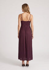 [Color: Merlot] A back facing image of a blonde model wearing a burgundy classic lace trim maxi dress with a v neckline, spaghetti straps, and side slits. 