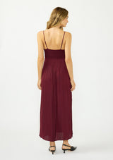 [Color: Merlot] A back facing image of a blonde model wearing a burgundy classic lace trim maxi dress with a v neckline, spaghetti straps, and side slits. 