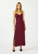 [Color: Merlot] A front facing image of a blonde model wearing a burgundy classic lace trim maxi dress with a v neckline, spaghetti straps, and side slits. 
