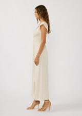 [Color: Natural] A side facing image of a brunette model wearing a beige linen blend maxi dress with short sleeves, a square neckline with tie detail, and a flowy skirt with a side slit. 