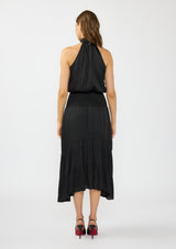[Color: Black] A back facing image of a brunette model wearing a black holiday halter maxi dress with a sleeveless design, smocked drop waist, and tiered skirt. This flowy satin dress is perfect for any special occasion and holiday events. 
