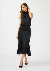 [Color: Black] A front facing image of a brunette model wearing a black holiday halter maxi dress with a sleeveless design, smocked drop waist, and tiered skirt. This flowy satin dress is perfect for any special occasion and holiday events. 