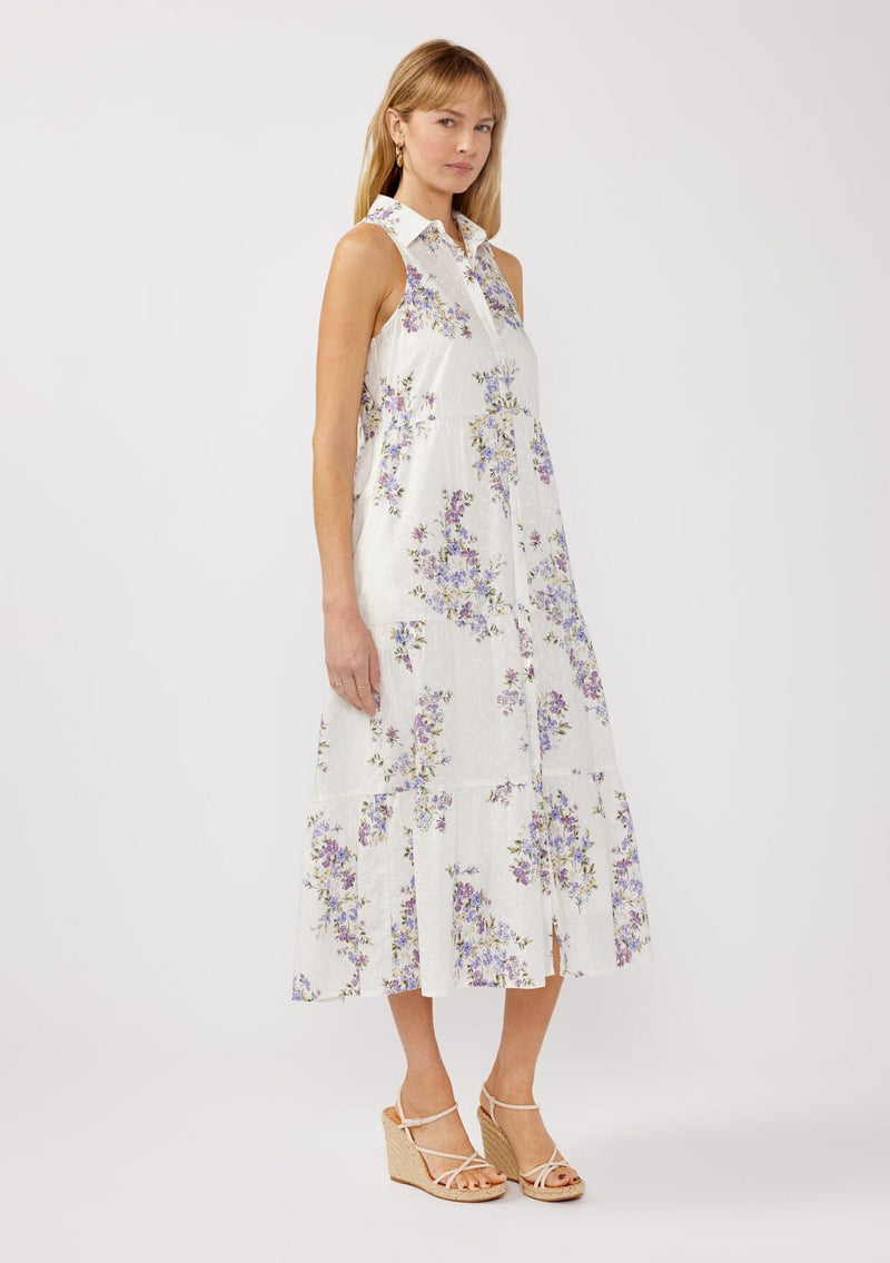 [Color: Off White/Lilac] A side-facing image of a blonde model wearing a sleeveless purple floral midi shirt dress. The dress features embroidered eyelets, a collared neckline, a button-front design, and a tiered skirt. Ideal for weddings, Easter, or other special occasions.