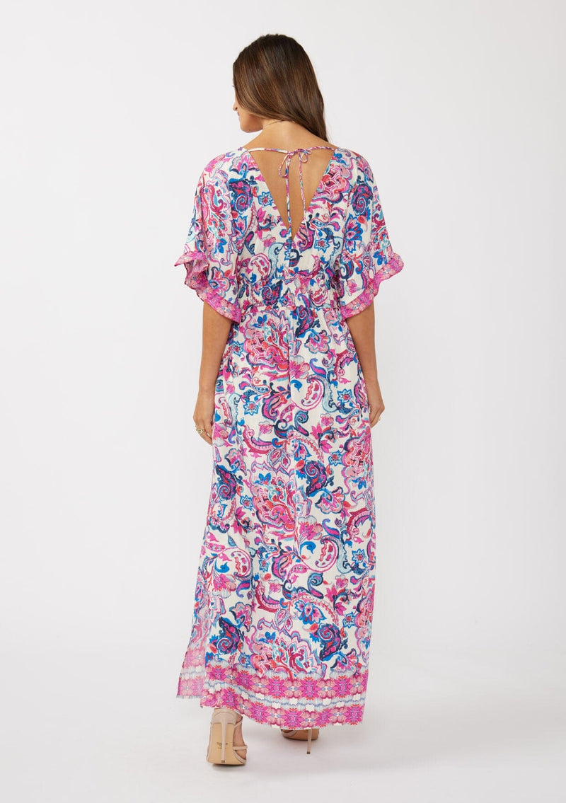 [Color: Natural/Dusty Pink] A back facing image of a brunette model wearing a pink and blue floral print kimono sleeve maxi dress with a ruffle trim, smocked waist, double v-neckline, and side slits. Perfect for spring special occasions. 