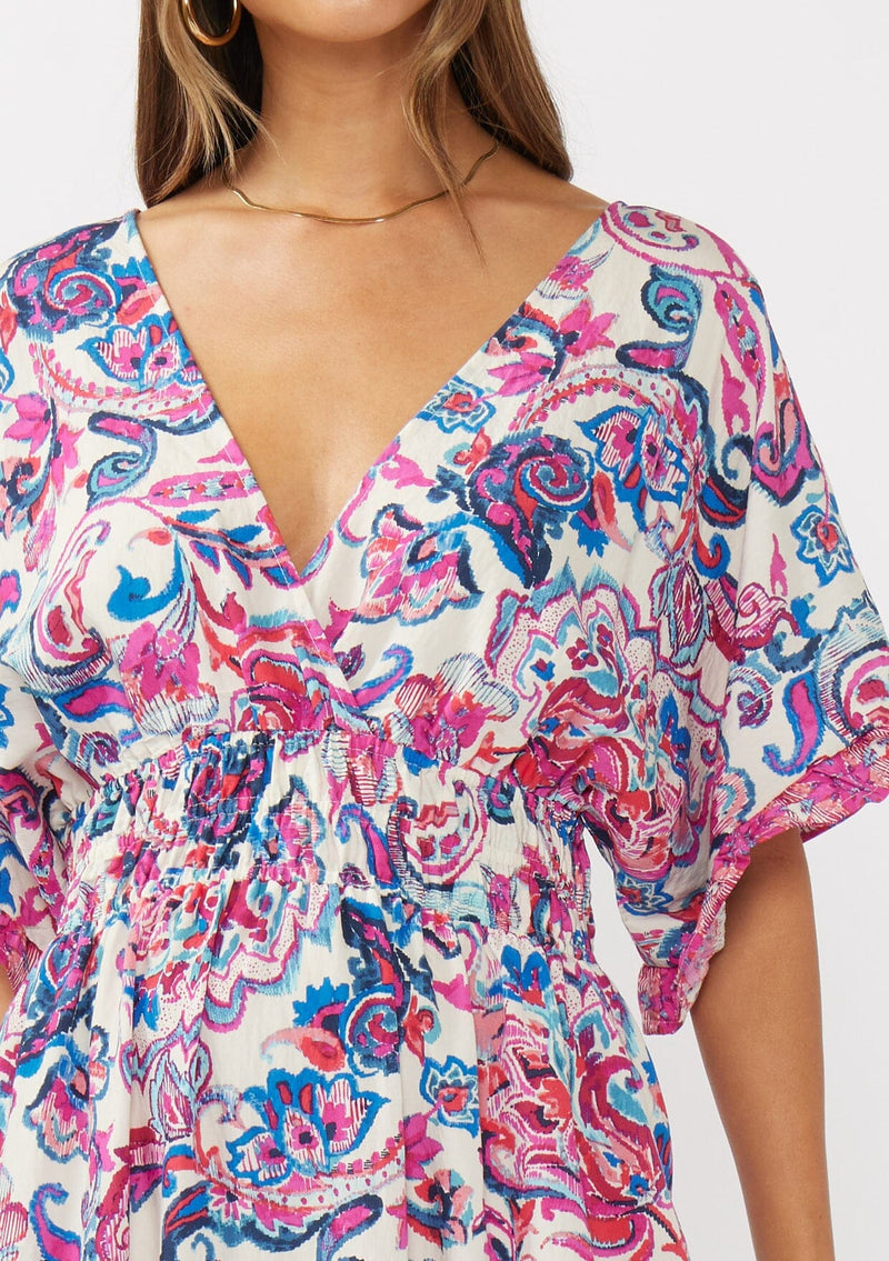 [Color: Natural/Dusty Pink] A detail image of a brunette model wearing a pink and blue floral print kimono sleeve maxi dress with a ruffle trim, smocked waist, double v-neckline, and side slits. Perfect for spring special occasions. 