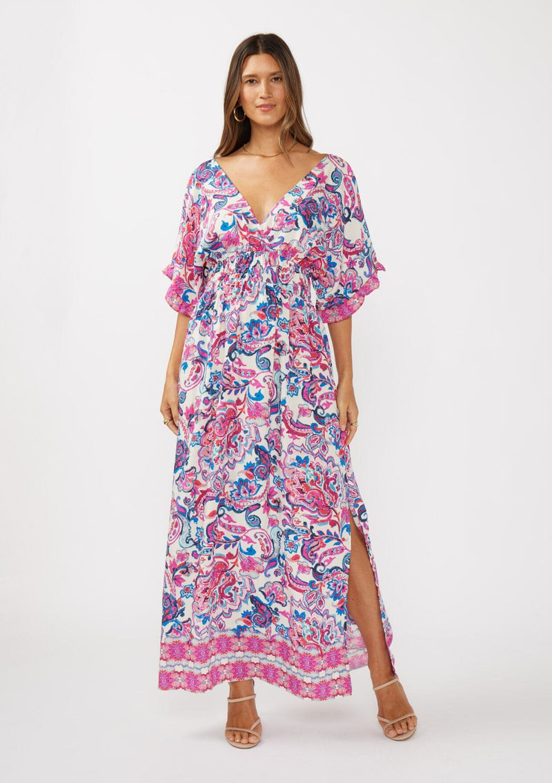 [Color: Natural/Dusty Pink] A front facing image of a brunette model wearing a pink and blue floral print kimono sleeve maxi dress with a ruffle trim, smocked waist, double v-neckline, and side slits. Perfect for spring special occasions. 