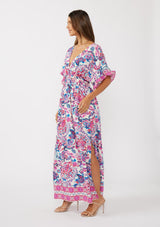 [Color: Natural/Dusty Pink] A side facing image of a brunette model wearing a pink and blue floral print kimono sleeve maxi dress with a ruffle trim, smocked waist, double v-neckline, and side slits. Perfect for spring special occasions. 