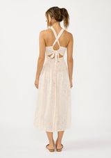 [Color Shell/Cream] A back facing image of a brunette model wearing a floral smocked midi dress with a sleeveless design, round neck, side pockets, and a cross back with tie detail. 